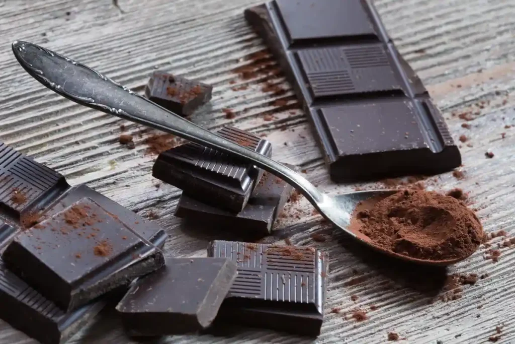 A dark chocolate bar alongside a spoon with cocoa powder, showcasing the rich ingredients.