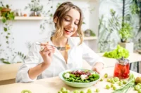 Woman enjoying a plate of healthy green food, including leafy vegetables and fresh greens, promoting a nutritious diet.