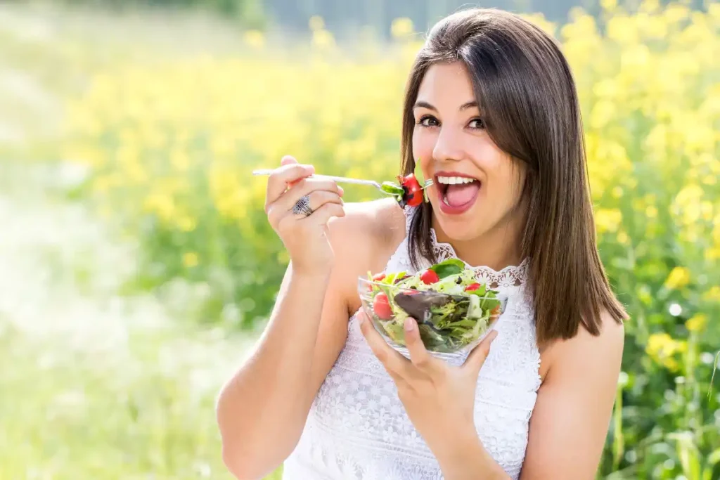 Attractive healthy girl enjoying a green salad outdoors, surrounded by nature, promoting a nutritious lifestyle.