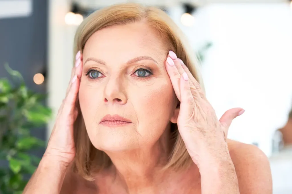Senior woman applying anti-wrinkle cream to her face in the bathroom as part of her skincare routine.