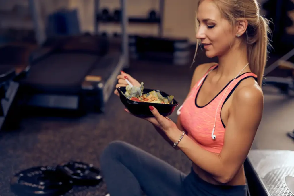 Woman eating a healthy meal, such as a salad or protein bowl, while taking a break at the gym after a workout.