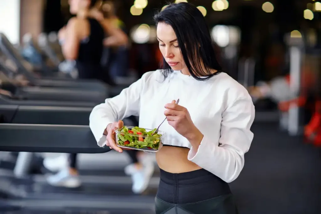 Sporty woman eating a fresh salad after her workout at the gym, refueling with healthy, nutritious food.