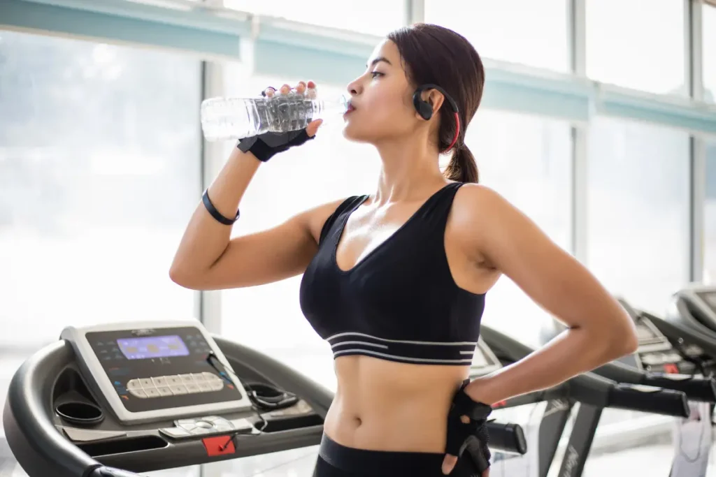 Sporty woman hydrating with a water bottle while taking a break at the gym.