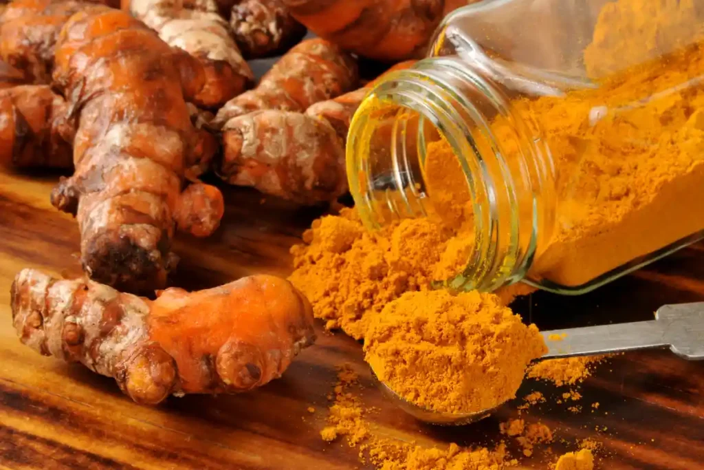 Turmeric powder inside a glass jar, accompanied by fresh turmeric roots, showcasing the natural spice.