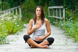 Woman sitting in meditation on a quiet country path, surrounded by nature.