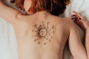 Woman lying on a bed, showing her astrology tattoo on her back.