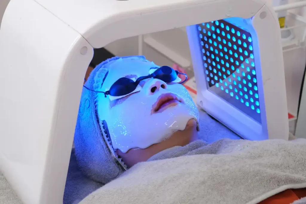 A woman receiving blue light skincare treatment in a spa, designed to improve skin health, reduce acne, and hydrate the skin with a moisturizing mask.