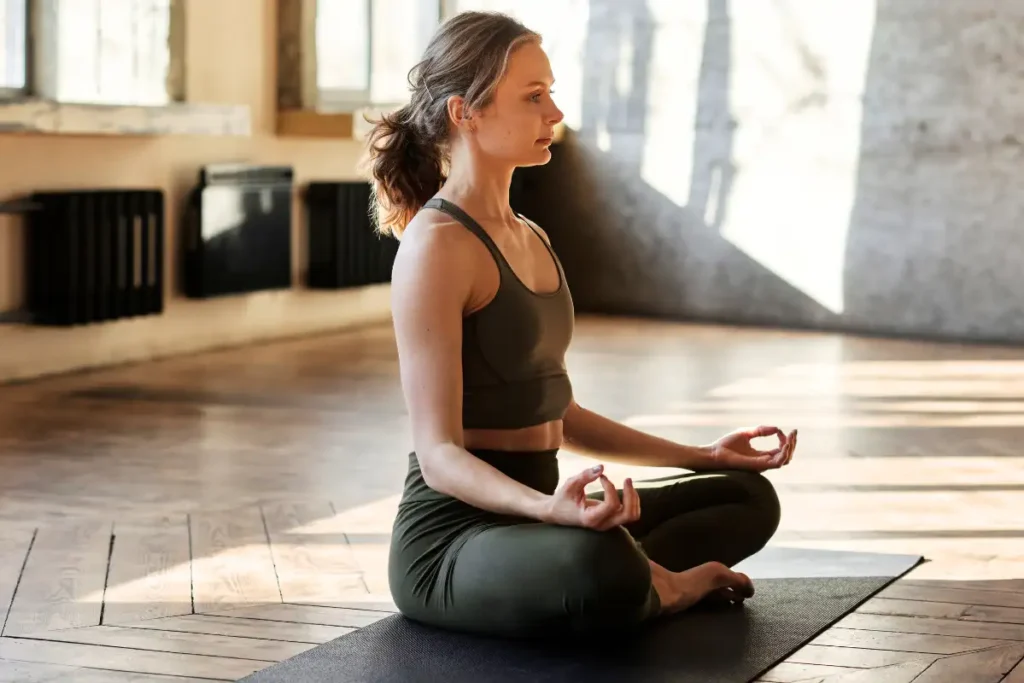 A woman practicing meditation in a yoga pose, sitting peacefully with her legs crossed and hands resting on her knees, focused on mindfulness.